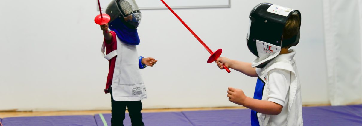 Students wearing protective clothing learn fencing in Tessa Afterschool class.