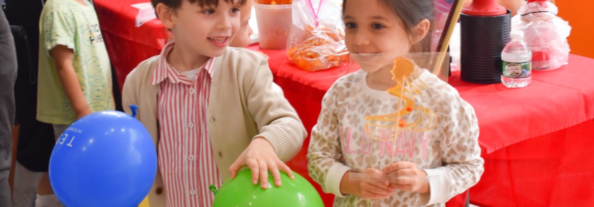 Two preschoolers delightfully hold balloons and sugar paintings to celebrate the Lunar New Year at Tessa International School in Hoboken, NJ.