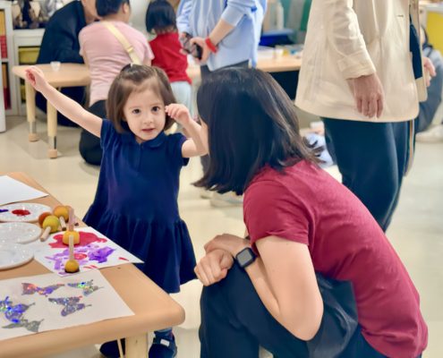 A toddler happily explaining to her mother the art activity during her IB PYP End-of-Unit Celebration