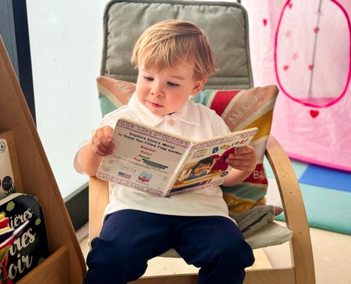 A PK2 toddler in Tessa International School's French Nursery Program read a book.